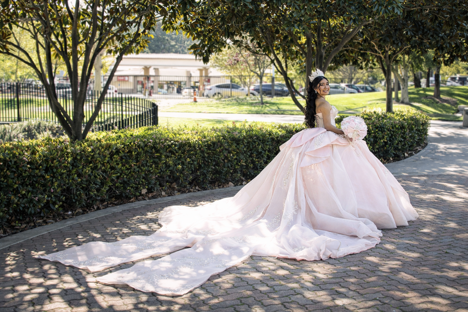Quinceañera in a pink gown with a long train in a sunlit park